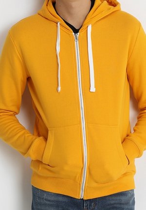 Sudadera con capucha amarilla con cremallera, hecha de tela suave, con cremallera frontal, cordones blancos y bolsillos tipo canguro. Textura lisa y ajuste relajado.