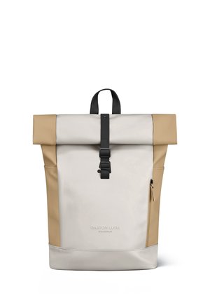 Sac à dos beige à rabat enroulable avec boucles et fermeture éclair noires, doté de poches latérales et de la marque "Gaston Luga Stockholm".