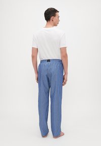 Gestreepte pyjamabroek in blauw, met verticale strepen in oranje en wit. Elastische tailleband met een logotag aan de achterkant. Lichtgewicht stof.