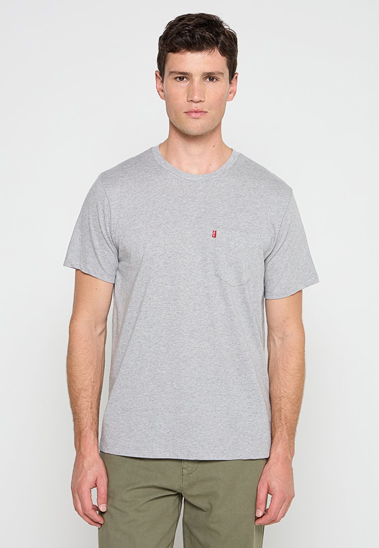 T-shirt en coton gris avec un col rond et des manches courtes. Présente un petit logo rouge sur la poche gauche de la poitrine. Design simple.