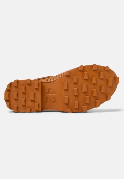 Rubber outsole in orange with prominent lugs for traction, featuring a textured surface and embossed logo design.