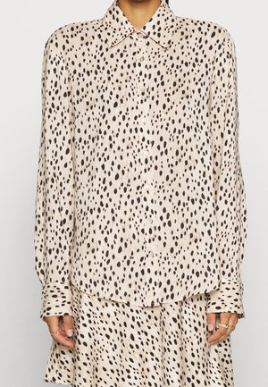 Skjortebluse med lange ærmer og knapper med cremefarvet baggrund og uregelmæssige sorte og brune pletter, kombineret med matchende nederdel.