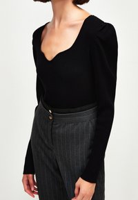 Czarny prążkowany top z długim rękawem, płytkim dekoltem w serek i bufionymi ramionami, zestawiony z wysokim stanem szarych spodni w prążki z podwójnymi guzikami.