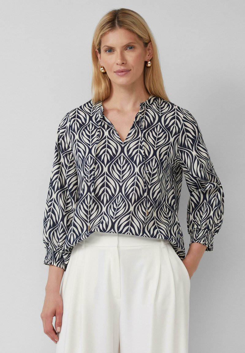 Bluse in Marineblau und Creme mit Blattmuster, V-Ausschnitt und gerüschten Ärmeln. Leichte Stoffqualität mit lockerer Passform.