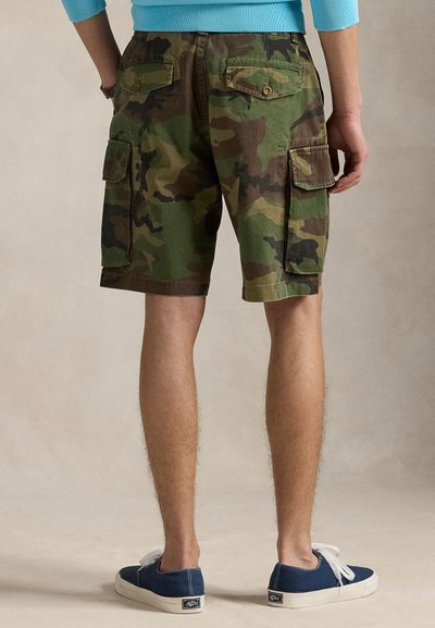 Cargo σορτς με καμουφλάζ σχέδιο, κατασκευασμένα από ελαφρύ ύφασμα, με πολλαπλές τσέπες και άνετη εφαρμογή. Φορεμένα με μπλε πάνινα αθλητικά παπούτσια.