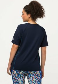 Camiseta deportiva navy de manga corta tipo raglán, con costuras en turquesa y detalle del logo en la manga izquierda.
