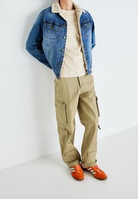 Denimjacka med shearlingkrage, beige t-shirt, khaki cargo-byxor med fickor och orangea sportskor med gröna ränder.