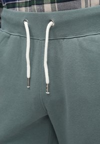 Φόρμες σε ανοιχτό γαλαζοπράσινο χρώμα με ριμπ ζώνη μέσης, λευκά κορδόνια και μεταλλικά άκρα. Μαλακή υφή και casual σχεδιασμός.