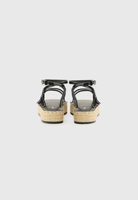 Sandalias de plataforma de charol negro con suelas de yute trenzado, múltiples correas y un hebilla ajustable en el tobillo. Superficie superior texturizada.