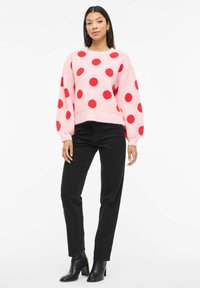 Roosa kampsun suurte punaste täppidega, ümara kaeluse ja volangvarrukatega. Kandmiseks mustad sirge säärega teksapüksid ja mustad kontsaga pahkluu saapad.