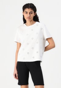 White cotton t-shirt with short sleeves, featuring floral cut-out designs. Paired with black bicycle shorts. Simple, casual design.