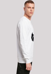 Hvid langærmet sweatshirt med et sort grafisk design på fronten, rund hals, ribbet manchetter og en afslappet pasform.