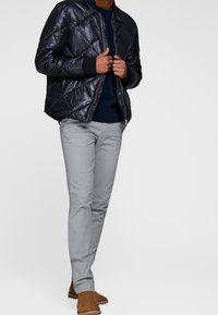 Czarna, ocieplana kurtka bomber z pikowaniem w kształcie rombów, zestawiona z jasnoszarymi, dopasowanymi spodniami i brązowymi botkami za kostkę.