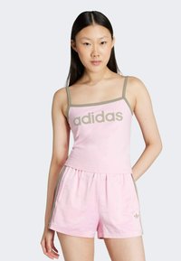 Rózsaszín pamut ujjatlan felső szürke részletekkel és "adidas" logóval, párosítva azonos rózsaszín sorttal, amelyen szürke oldalsávok és zsebek találhatók.