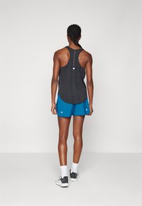 Canotta atletica nera con design a schiena a vogatore e cerniera riflettente, abbinata a pantaloncini blu con dettagli bianchi e vestibilità ampia.