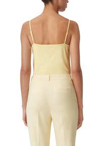 Ljusgul spaghetti strap top med en slät textur, i kombination med ljusgula skräddarsydda byxor med bakfickor och rak passform.