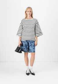 Stripete oversized topp i svart og hvitt med vide ermer, kombinert med blå kamuflasje denimshorts. Tilbehøret inkluderer en svart håndveske og hvite sokker med sorte skohelter.