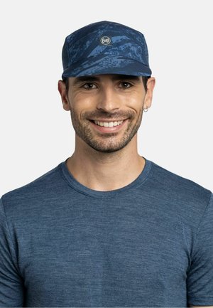 Smiling man wearing a blue patterned cap with a Buff logo and a matching blue crew neck shirt against a plain background.