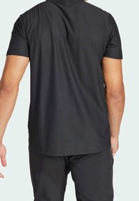 T-shirt nera a maniche corte, tessuto liscio con una leggera texture, vista posteriore che mostra lo scollo arrotondato e il design semplice. Nessun logo o motivo visibile.