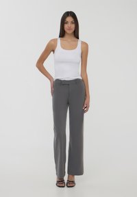 Biała koszulka na ramiączkach, szare eleganckie spodnie z pętelkami na pasek, prosty krój, gładka struktura tkaniny oraz czarne sandały z cienkimi paskami.