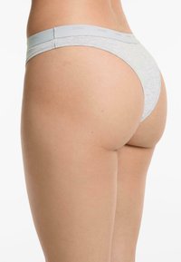 Ljusgrå stringtrosa i lingerie med mjuk elastisk midjeband som har varumärkesnamnet, slät tygtextur och minimal baktäcka design.