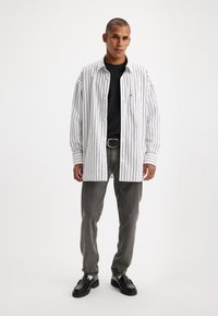 Stripet langermet skjorte i hvit og svart, kombinert med en svart t-skjorte og grå jeans. Brukt med svarte sko, med en klassisk design.