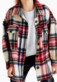 Veste à carreaux en rouge, rose, bleu et crème, fabriquée en mélange de laine. Dispose de deux poches poitrine et de boutons noirs. Coupe décontractée et manches longues.