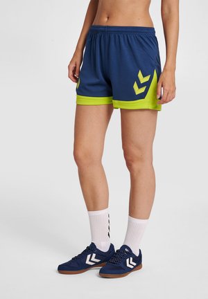 Marineblauwe sportshorts met neon groene accentueringen, voorzien van een gestructureerde stof en chevronpatronen aan de zijkanten, gecombineerd met marineblauwe schoenen en witte sokken.