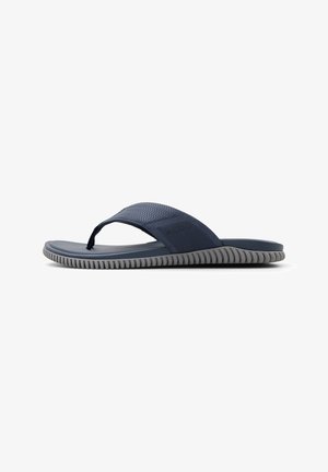 Sinivihreä flip-flop, jossa on teksturoitu hihna ja harmaa pohja. Hihnassa on hienovarainen logo sivussa ja sahalaitakuvio.