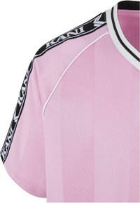 Pink sports jersey with vertical stripes, black and white band at the collar, and branded black and white tape on the shoulder.