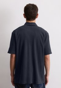 Korte mouwen polo in donker marineblauw met verticale ribstructuur, een platte kraag en een rechte onderkant. De achterkant toont een eenvoudig ontwerp.