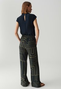 Marineblauw blouse met een sleutelgat achterkant, gecombineerd met wijde broek met een geometrisch groen en zwart patroon. Soepele textuur, elastische tailleband.