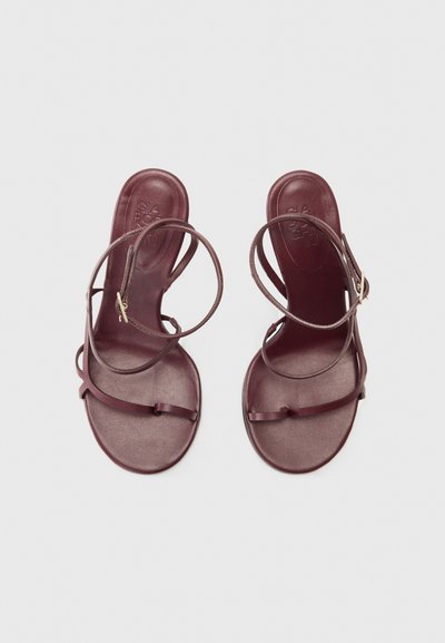Burgundské ploché sandály s několika tenkými pásky, hladkou podrážkou a minimalistickým designem. Obsahují malou přezku pro nastavení.