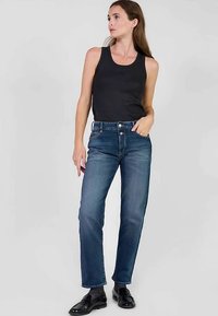 Donkerblauwe spijkerbroek met rechte pijpen, hoge taille en vijf zakken, gecombineerd met een zwart hemdje en zwarte schoenen.