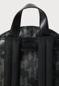Black backpack featuring textured fabric with a green abstract pattern, complemented by sturdy black leather accents and thick straps.