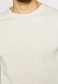 Ljust beige stickad tröja med rund halsringning. Tyget har en fin struktur och visar upp en minimalistisk design utan synliga mönster eller accenter.