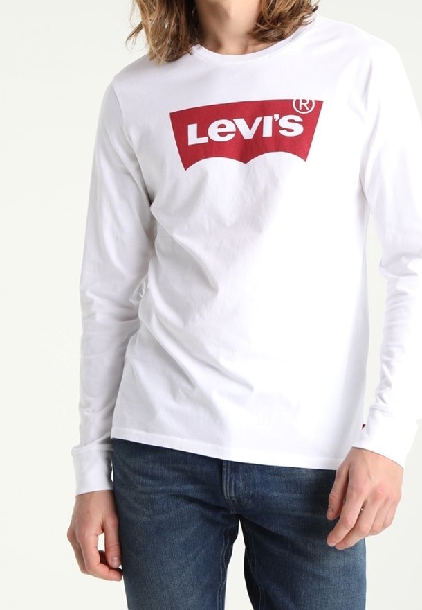 Weißes Langarmshirt mit rotem Levi's-Logo auf der Brust, aus Baumwolle, kombiniert mit blauen Denim-Jeans. Einfaches Design, Rundhalsausschnitt.