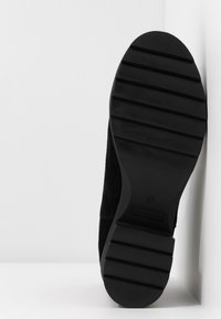 Suela de zapato de ante negro con un fondo de goma texturizada y ranuras horizontales para tracción, además de un diseño de punta suave y redondeada.