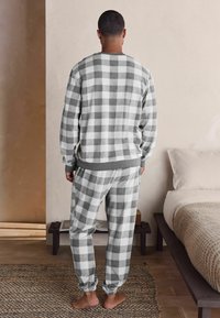 Grau-wei�ßes kariertes Loungewear-Set. Weicher Stoff, lockere Passform, langärmliges Oberteil mit Rippbündchen und tapered Hosen mit elastischen Bündchen.