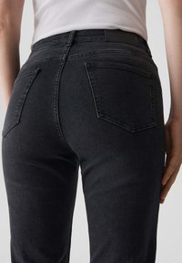 Jeans neri in denim con un taglio a vita alta, dotati di due tasche posteriori e una texture liscia. La cintura è semplice, senza branding visibile.