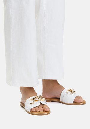 Białe sandały na płaskiej podeszwie, z szerokim paskiem i złotym łańcuszkiem z przodu. Podeszwa w kolorze brązowym, płaska, z odkrytymi palcami.