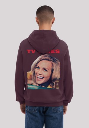 Burgunderfarbene Kapuzenjacke mit einem Grafikdesign eines Vintage-Fernsehmagazins auf dem Rücken, das eine lächelnde Frau mit blonden Haaren zeigt, sowie Text in Rot und Gelb.