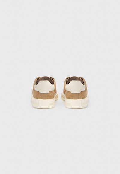 Καφέ suede αθλητικά παπούτσια με κρέμα και λεπτομέρεια στη φτέρνα από καουτσούκ. Μινιμαλιστικός σχεδιασμός, στρογγυλεμένο σχήμα και λεία υφή.
