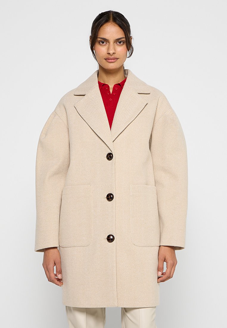 Beżowy płaszcz w jodełkę z klapami, trzema dużymi brązowymi guzikami i dwoma przednimi kieszeniami; charakteryzuje się luźnym krojem i teksturowanym materiałem.