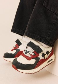 Białe i czerwone sneakersy z czarną gumową podeszwą, z emblematem Myszki Miki i rzepami; teksturowany materiał i zabawny design.