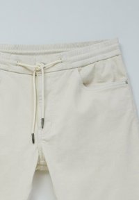 Joggers de color beige claro hechos de una suave mezcla de algodón. Cuentan con una cinturilla elástica con cordón y dos bolsillos laterales con costuras sutiles.