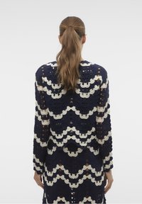 Abito a maniche lunghe all'uncinetto in navy e crema, caratterizzato da motivi a conchiglia e una trama aperta. La vista posteriore mostra dettagli e design intricati.
