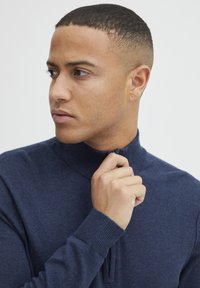 Marinblå zip-krage tröja tillverkad av mjukt material, med ribbade ärmslut och en slät yta, samt en halvdragkedja för justerbar passform.