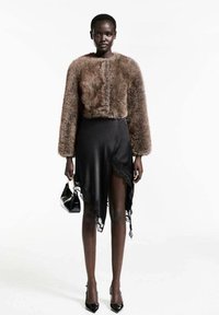 Faux fur brun kort jacka, svart satin asymmetrisk kjol med spetskant, och svarta högklackade skor, tillsammans med en liten handväska.