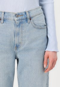 Light blue denim jeans with a relaxed fit, featuring a button closure, five-pocket design, and slight fading on the fabric.